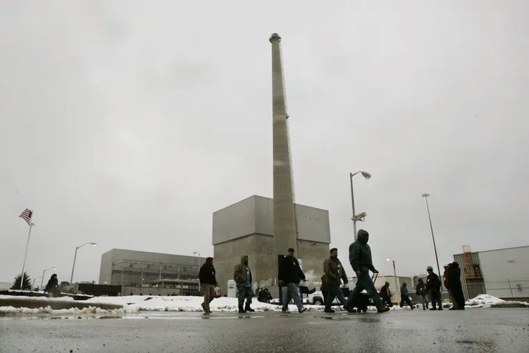 Workers walk in front of a large square building that houses the nuclear reactor at the Oyster Creek nuclear plant in Lacey Township, N.J.