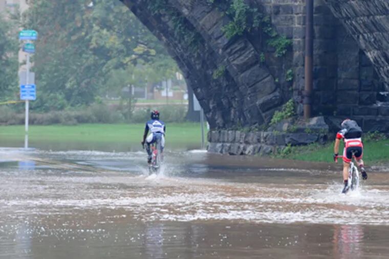 Bicyclists apparently unperturbed by the overflowing Schuylkill pedal west along Kelly Drive. (Clem Murray / Staff Photographer)