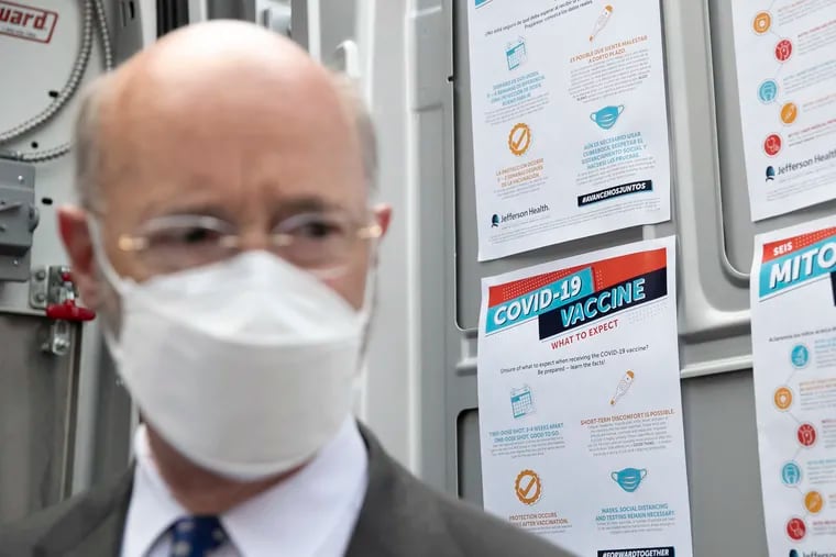 Vaccine posters are seen behind Gov. Tom Wolf while he tours a Philadelphia clinic on Friday.