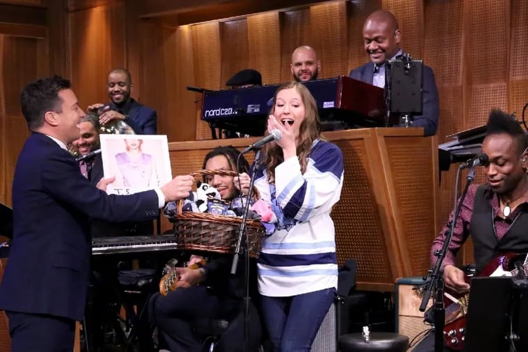 Host Jimmy Fallon presenting a gift basket to Villanova Pep Band piccolo player Roxanne Chalifoux, who played with the Roots on March 23, 2015.