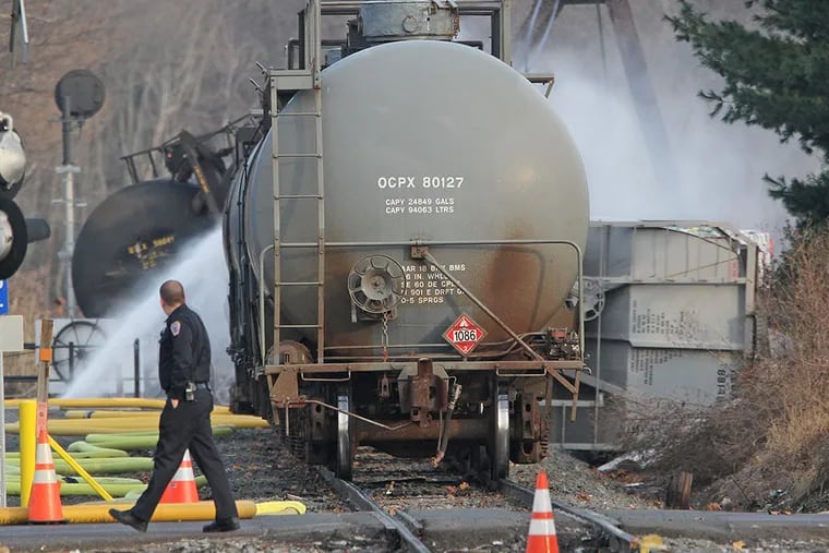 A Police officer walks by and takes a llok as water is being sprayed onto the tanker cars that were derailed in Paulsboro, NJ in 2012. ( MICHAEL BRYANT / Staff Photographer )
