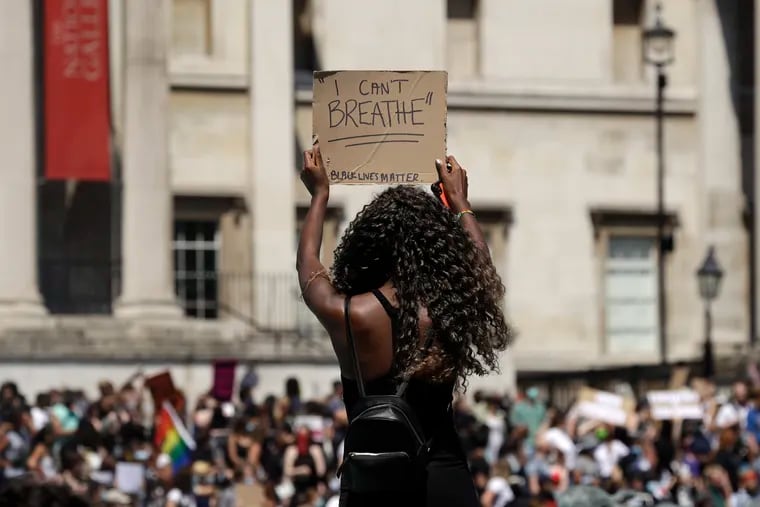 A woman holds up a banner as people gather in Trafalgar Square in central London on Sunday, May 31, 2020 to protest against the recent killing of George Floyd by police officers in Minneapolis that has led to protests across the US.