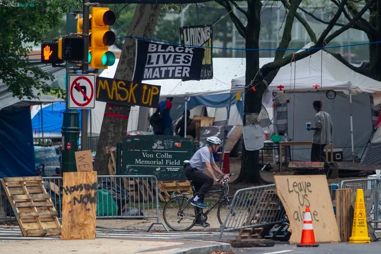 A cyclist rides by the homeless encampment last month on the Benjamin Franklin Parkway. The city and encampment organizers reached an agreement Tuesday evening to amicably disband the site by the end of the week.