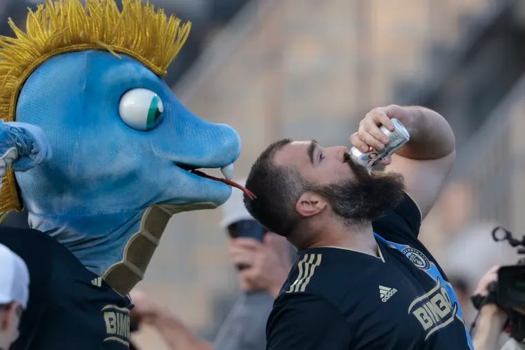 Eagles star Jason Kelce chugged a beer on the field in front of Union mascot Phang (left) after being the Union's celebrity pregame drummer at Wednesday's win over Charlotte FC.