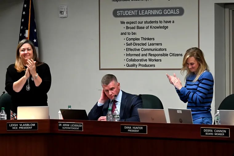 Central Bucks School District Superintendent Abram Lucabaugh is applauded by school board president Dana Hunter right and vice president Leigh Vlasblom left after criticizing false narratives circulating in the community during a May 10 board meeting The board is now considering a library policy that some fear could result in sweeping restrictions on books available to students