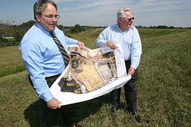 On the Gloucester County site, lawyer Robert W. Bucknam Jr. (left) and Bill Geary, president of Clean Harbors, hold plans for the solar array. (CHARLES FOX / Staff Photographer)