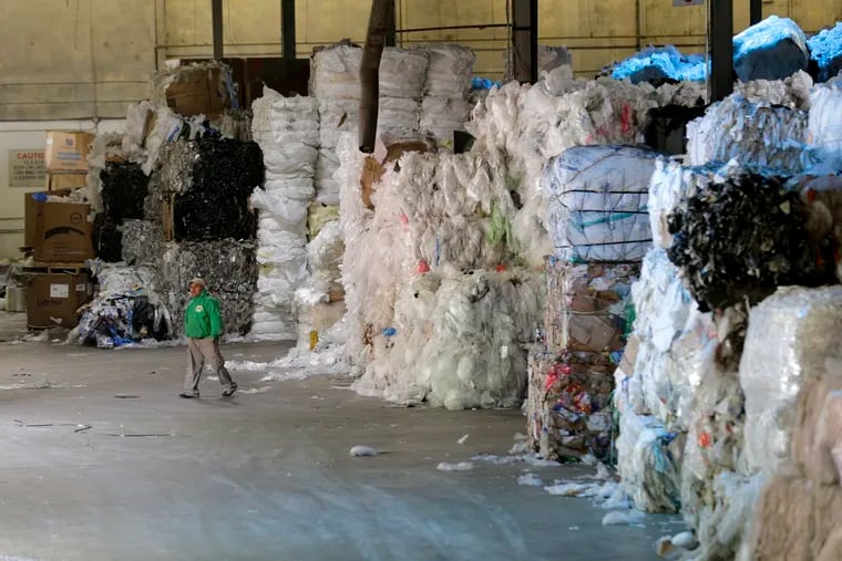 In this May 7, 2019 photo, a man walks under towers of recyclables at a GDB International warehouse in Monmouth Junction, N.J. A decision by China’s government to restrict imports of wastepaper and plastic that has disrupted U.S. recycling programs has also spurred investment in American plants that process recyclables.