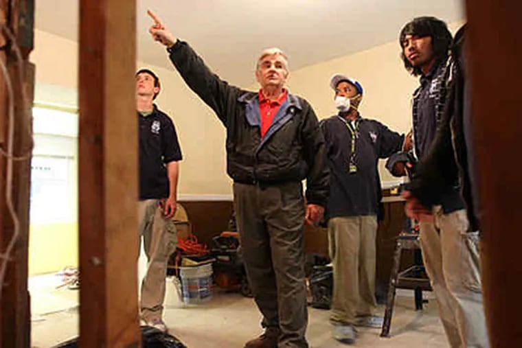 Sam Ginsburg, a retired Bok High School teacher who volunteers with Sunrise Philadelphia Inc., shows students where to frame a living-room wall in the former South Philadelphia drug house they are rehabbing. (Michael Bryant / Staff)