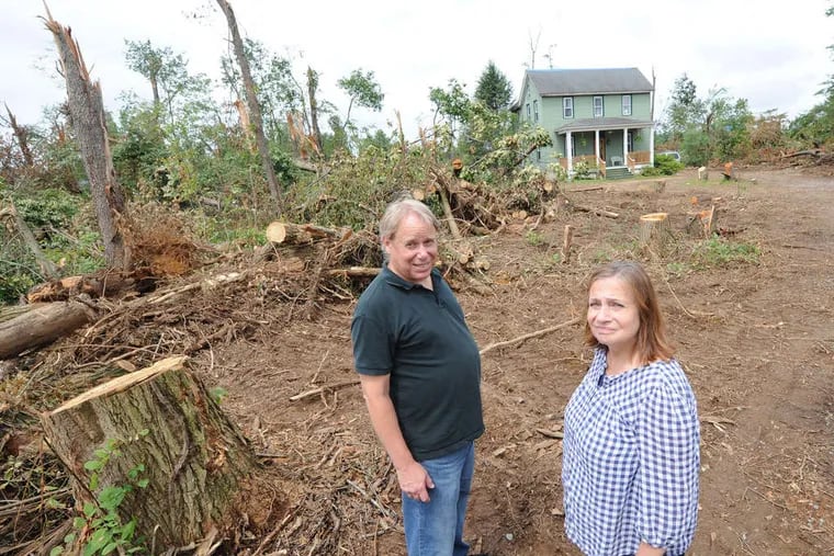 Rob and Pam Kafka stand amid trees downed by a June 23 storm that devastated Clarksboro and other parts of Gloucester County. In the background is the home of their daughter Molly.