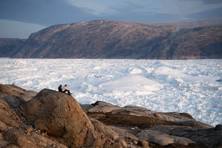 In this Aug. 16, 2019, photo, New York University student researchers sit on a rock overlooking the Helheim glacier in Greenland.  U.S. President Trump announced his decision to postpone an early September visit to Denmark by tweet Tuesday Aug. 20, 2019, after Danish Prime Minister Mette Frederiksen dismissed the notion of selling Greenland to the U.S. as "an absurd discussion."