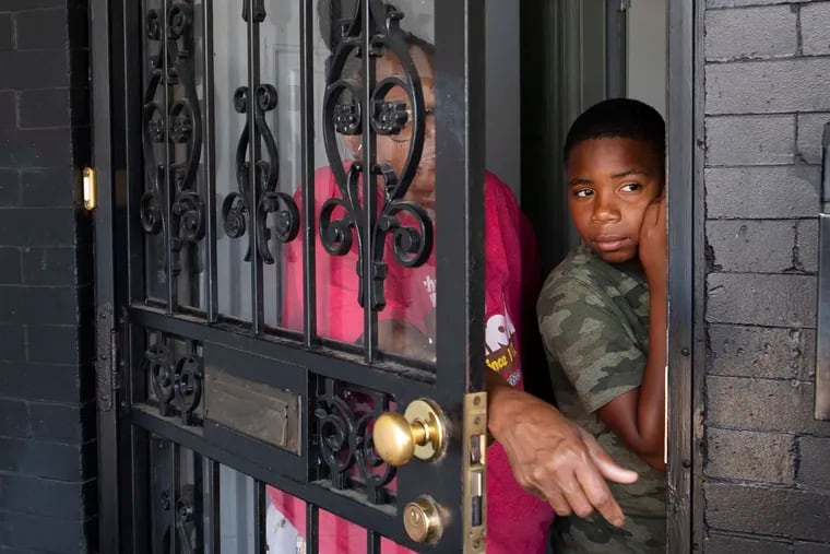 Carolyn and her grandson (they did not want their last names published for security reasons) look out from the front door of their home across from Charles Baker playground at 54th Street and Landsdowne Avenue in West Philadelphia on Sunday, a day after seven people were shot during a basketball game.