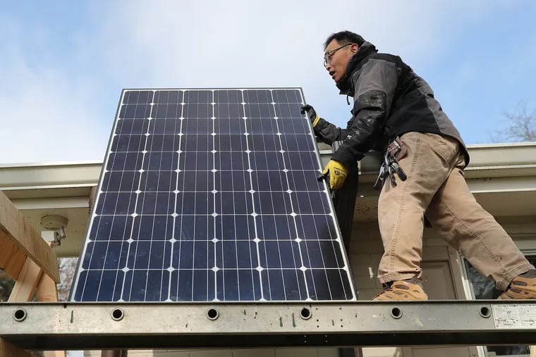 John Y.K. Lee moves a solar panel to the edge of his roof in Haverford.