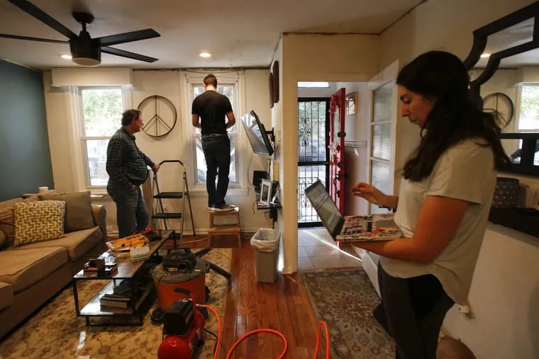 Samantha Mayo (right) looks at her computer as her fiance Kevin Buttery screw a cornice in their South Philadelphia home as his father Alex Buttery (left) watches on Saturday, November 4, 2017. YONG KIM / Staff Photographer
