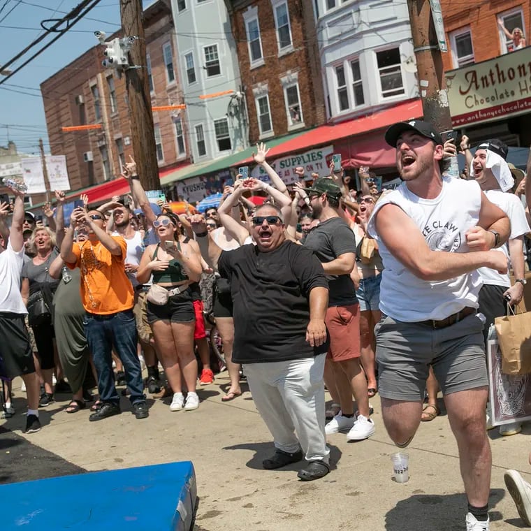 The crowd cheers as a group of men with Pace Roofing LLC compete in the grease pole contest at the South 9th Street Italian Market Festival in Philadelphia on Saturday, May 21, 2022. The festival return to 9th Street this weekend Saturday, May 18 and Sunday, May 19.