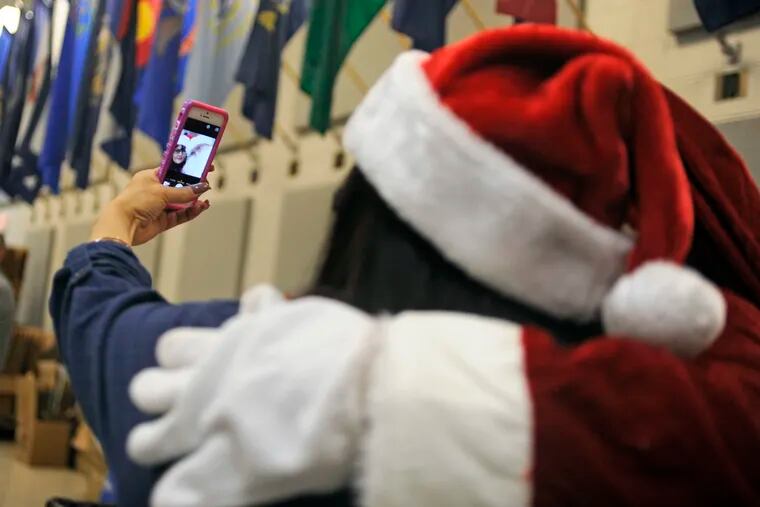 Walmart employee Sue-Link Huertas takes a selfie with Santa. Walmart workers and Lockheed Martin employees from the company's Moorestown campus helped members of the 99th Regional Support Command, where the event was held, hand out the meals. TOM GRALISH / Staff Photographer