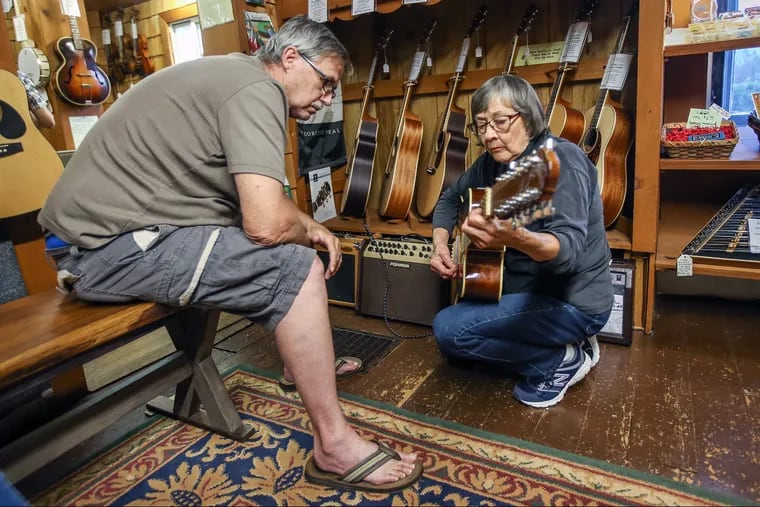 Jackie Dieterichs, right, who started the Bucks County Folk Music Shop with her husband Karl, strums a 12 string acoustic electronic cutaway guitar for prospective buyer Donald Corum, left, in their shop in New Britain, PA.