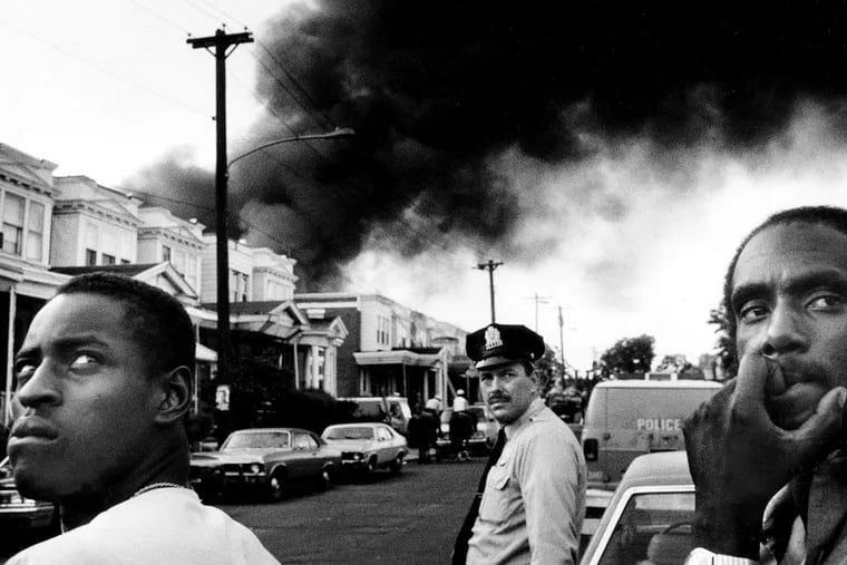 Smoke pours out over Osage Avenue after police dropped a bomb from a helicopter onto the roof of the MOVE house in West Philadelphia - and firefighters were ordered to let the fire burn. Six adults and five children died in the confrontation that day, May 13, 1985, and 61 surrounding homes were destroyed. (TOM GRALISH / Staff Photographer)