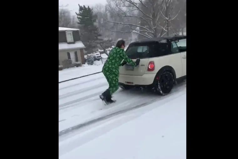 A screenshot of a video of Cary McClain, a Main Line defense attorney, pushing a Mini Cooper up a hill while wearing a weed suit.