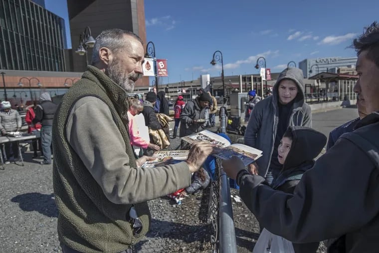 Tom Martin, left, hands out books as they wait in line for food in a parking area near MLK Blvd on  Feb. 18. The Camden County Pop Up Library distributes free books to homeless and other folks in need downtown and at other sites in Camden.
