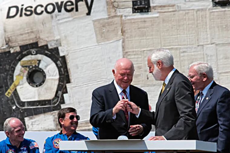 Former astronaut and Sen. John Glenn, center, accepts a pen before signing the handover paperwork as the space shuttle Discovery is officially welcomed to the Udvar-Hazy center in Dulles, Va. Handing him the pen is Smithsonian Secretary Wayne Clough.  At far right is Air and Space Museum Director J.R. Dailey. (BILL O'LEARY / The Washington Post)