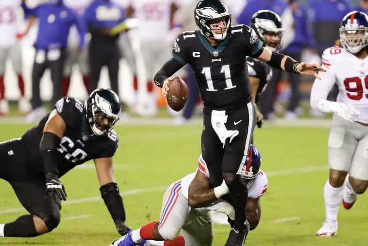Eagles quarterback Carson Wentz looks for a receiver while getting held by New York Giants linebacker Markus Golden on Thursday, October 22, 2020.