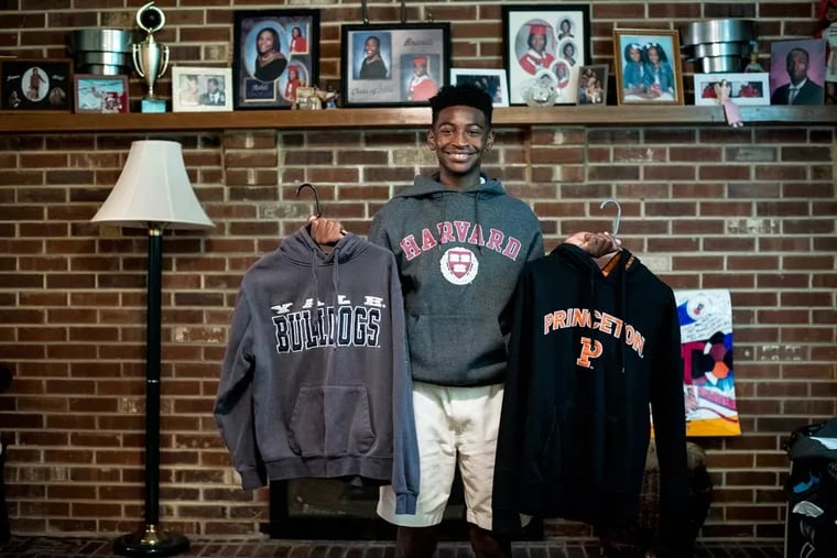 Calvin R. Bell III of Pennsauken, 14, wears a Harvard University sweater while holding university sweaters for Yale and Princeton.