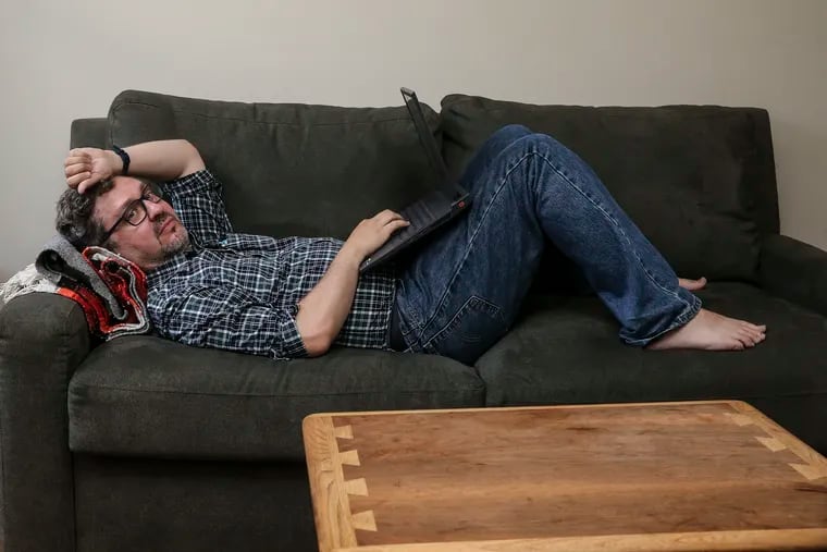 Jonathan Lipman tries to work on the couch in his home office in South Philadelphia on Wednesday, July 13, 2022. He's had long COVID for more than two years, and can only work at most 4-5 hours per day.