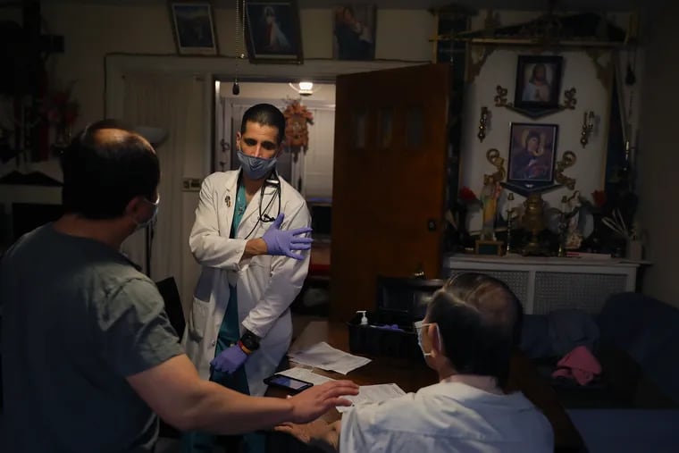 Nurse-practitioner Tarik Khan (center) motions to his left arm as he prepares to give a second dose of the Moderna COVID-19 vaccine to Khanh Pham (right), 89, at his home in Southwest Philadelphia earlier this month.
