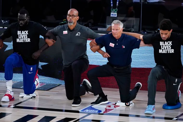 Phoenix Suns head coach Monty Williams (second from left) and Sixers coach Brett Brown (second from right) kneel with others during the national anthem before the start of a recent game.