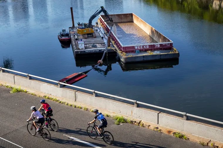 Recreational cyclists along Martin Luther King Drive over river as Texas-based Dredgit is pumping the muck from north side of Schuylkill river in August 2022.