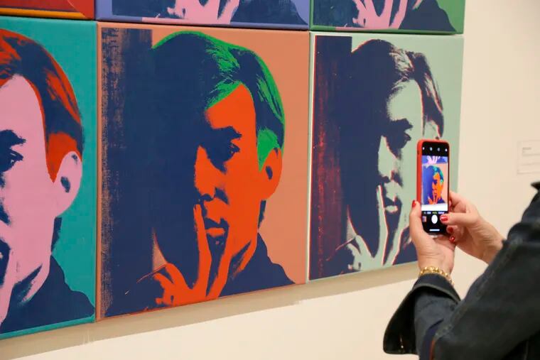 In this photo taken Wednesday, May 15, 2019, a woman records one of a series of self portraits at the exhibition, "Andy Warhol _ From A to B and Back Again", in San Francisco. A retrospective of Andy Warhol's work on display at the San Francisco Museum of Modern Art captures his use of artwork to give his subjects personas the way people do now using social media.   (AP Photo/Eric Risberg)