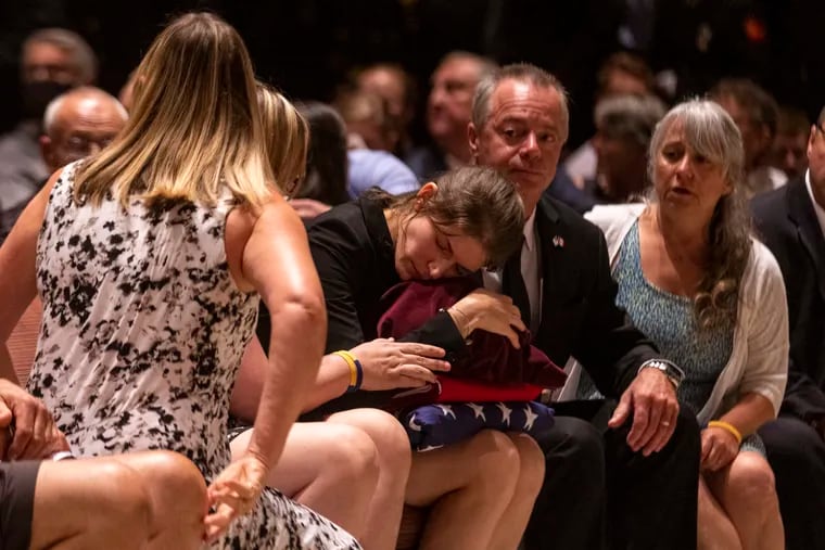 Melissa Richard-Greenblatt lays her head down while holding the urn containing the ashes of her husband, Sean DeMuynck, toward the end of his memorial service at Lower Merion High School on Saturday. The firefighter died in the line of duty when he became trapped on the third floor of a house on July 4.