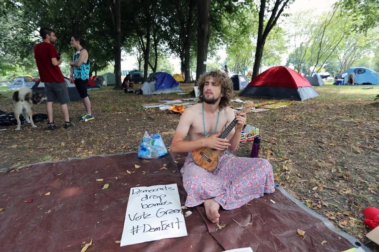 Tom Moore of Marion, Mass., wakes up with a tenor ukulele singing Bob Marley's "One Love" as dozens of protesters camp, sleep, meet and eat in FDR Park during the DNC at the Wells Fargo Center in Philadelphia.