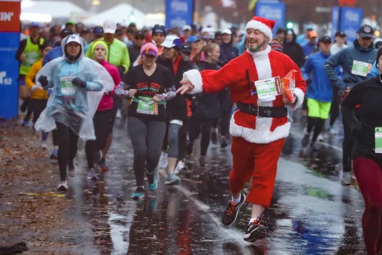 A runner dressed as Santa Claus throws candy to the crowd as he begins his race in the Philadelphia Marathon on the Benjamin Franklin Parkway on November 24, 2019.