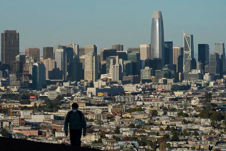 A person wearing a mask walks in front of the skyline on Bernal Heights Hill during the coronavirus pandemic in San Francisco. The first numbers from the 2020 census show southern and western states gaining congressional seats. The once-a-decade head count shows where the population grew during the past 10 years and where it shrank.