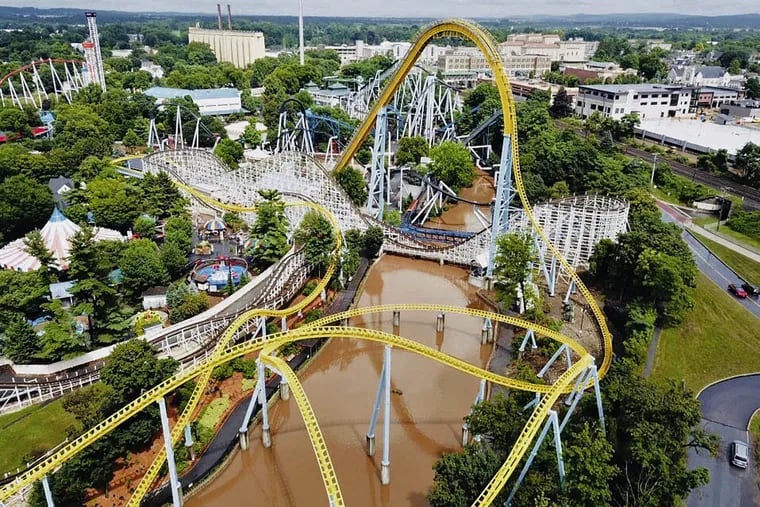 In this Monday, July 23, 2018, aerial image provided by The Wyse Choice photography in Hershey, Pa., muddy brown floodwaters in Spring Creek flow beneath the Skyrush roller coaster, in yellow, and the Comet roller coaster, in white, at the Hersheypark theme park in Hershey, Pa.