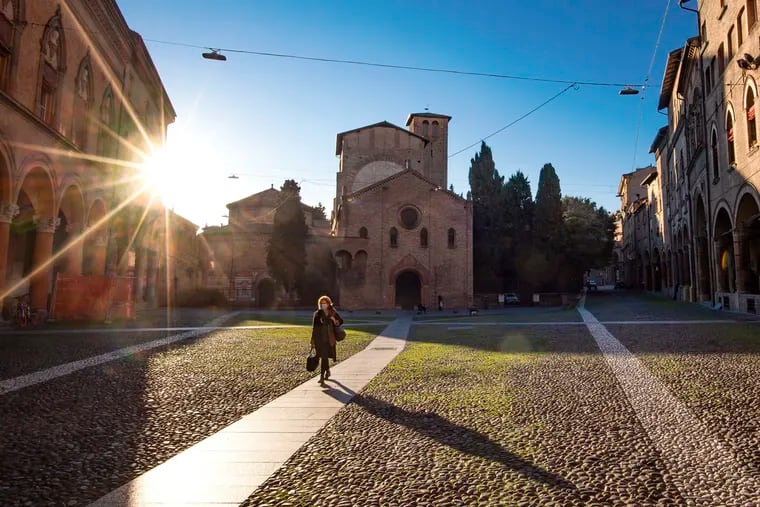A woman walks past the Basilica of Santo Stefano, in Bologna, Italy, Wednesday, March 11, 2020. In Italy the government extended a coronavirus containment order previously limited to the country’s north to the rest of the country beginning Tuesday, with soldiers and police enforcing bans. For most people, the new coronavirus causes only mild or moderate symptoms, such as fever and cough. For some, especially older adults and people with existing health problems, it can cause more severe illness, including pneumonia.