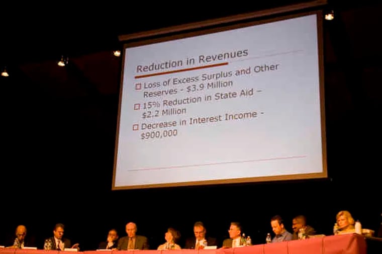 A PowerPoint presentation hangs over the Cherry Hill school board, showing revenue decreases the district will have to absorb.