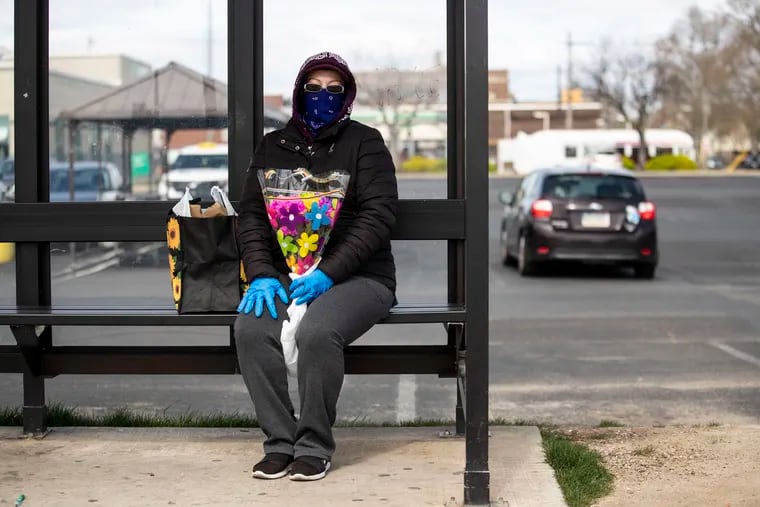 Sonia Morales, of South Philadelphia, wears a protective bandana and gloves while waiting at the bus stop in South Philadelphia.