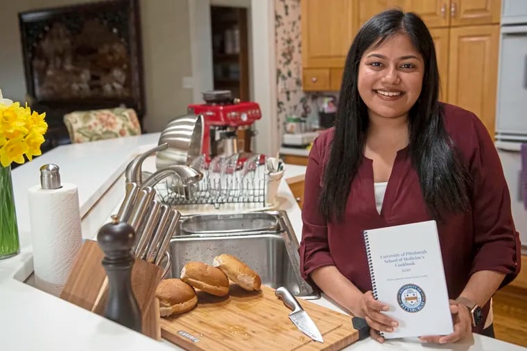 Eva Roy, a third-year medical student at University of Pittsburgh, holds the "University of Pittsburgh School of Medicine's Cookbook 2020," on Saturday, April 3, 2021, in her kitchen in Upper St. Clair. (Emily Matthews/Pittsburgh Post-Gazette/TNS)
