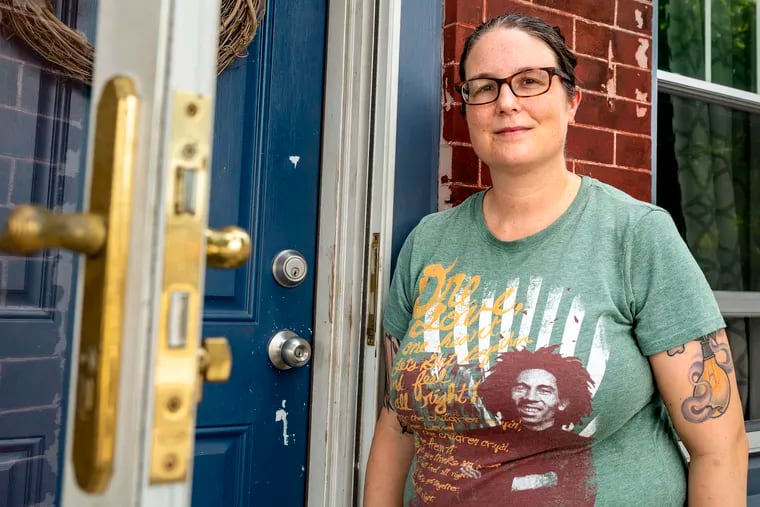 Natalie Shaak poses on her stoop with the temporary front door and storm door of her Port Richmond home.