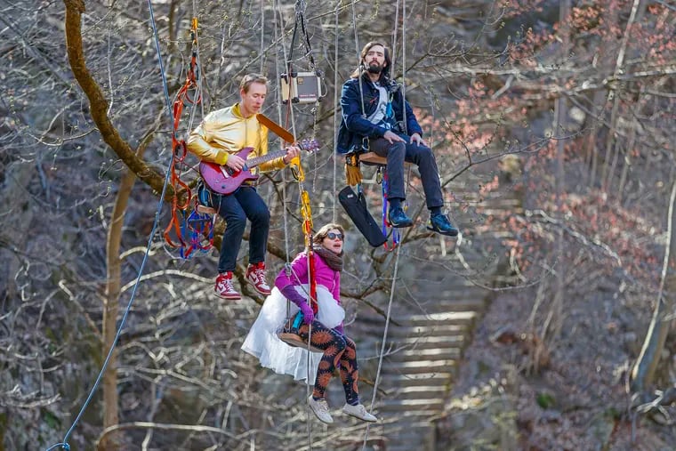 Climbers and musicians Colin Doyle (left), Anais Naharro-Murphy, and Willis Kuelthau play instruments and sing sitting on swings attached to a large tree limb overhanging the Wissahickon Creek on Monday April 1, 2019.