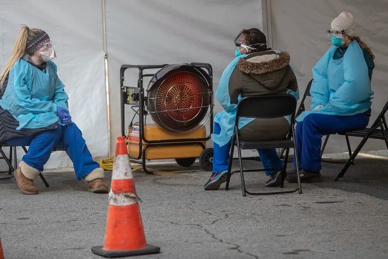 Thomas Jefferson medical personnel sit around a space heater under their tent at the coronavirus swab testing facility at 10th and Sansom Street.