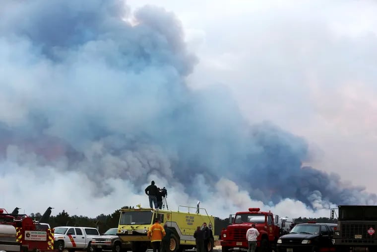 Spectators watch as the Spring Hill fire and backfire burns in Woodland Township, N.J., Sunday, March, 31, 2019. Authorities say fire whipped by high winds has spread over thousands of acres of state forest land in the Pinelands of New Jersey.  (Ed Murray/NJ Advance Media via AP)
