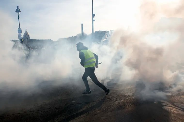 A yellow vest protester runs amid tear gas during scuffles with riot police officers Saturday, Feb.16, 2019 in Paris. Hundreds of yellow vest protesters marched through Paris, one of seven scattered demonstrations in the French capital Saturday, for the 14th straight weekend. (AP Photo/Thibault Camus)
