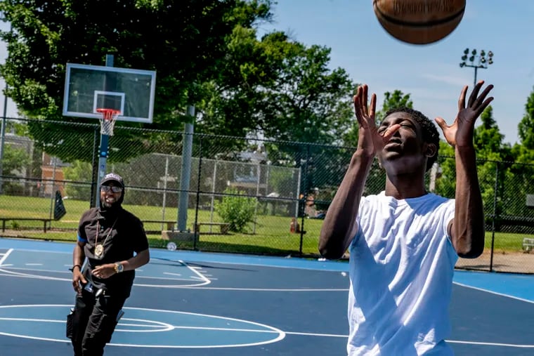 Musa Kane (right), 15, plays basketball at the Francis Myers Recreation Center in Kingsessing on Monday. Kane said he goes home before sunset every night to stay safe, but thinks other teens would find a way around an earlier city curfew this summer.