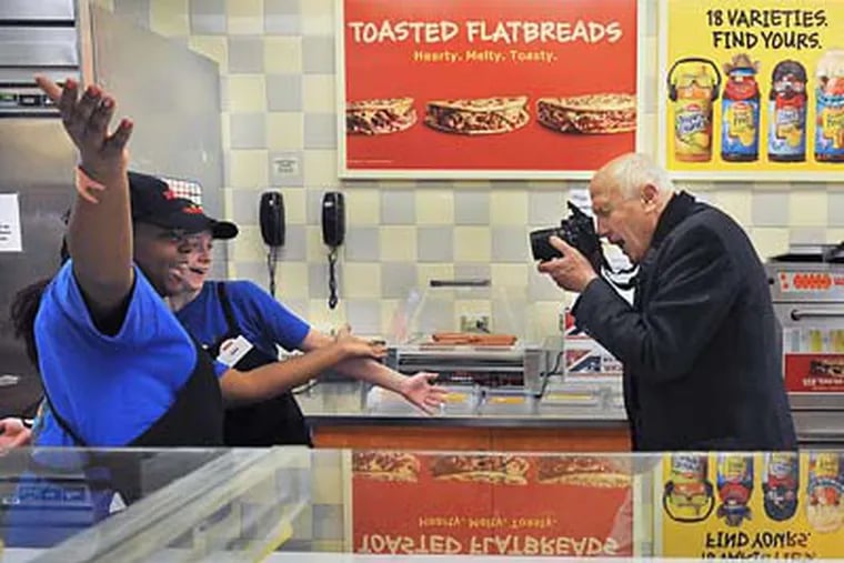 At the first ever Wawa store that opened in 1964 on MacDade Boulevard in Folsom, Don Price (right) takes photos of employees Lakisha Staten (left) and Cera Davis. Wawa is marking its 45th anniversary. (Sharon Gekoski-Kimmel / Staff Photographer)