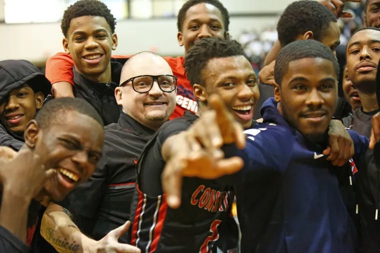 Constitution players celebrate around coach Rob Moore (with glasses) after defeating Holy Cross, 69-64, in a PIAA Class 2A basketball semifinal Saturday.