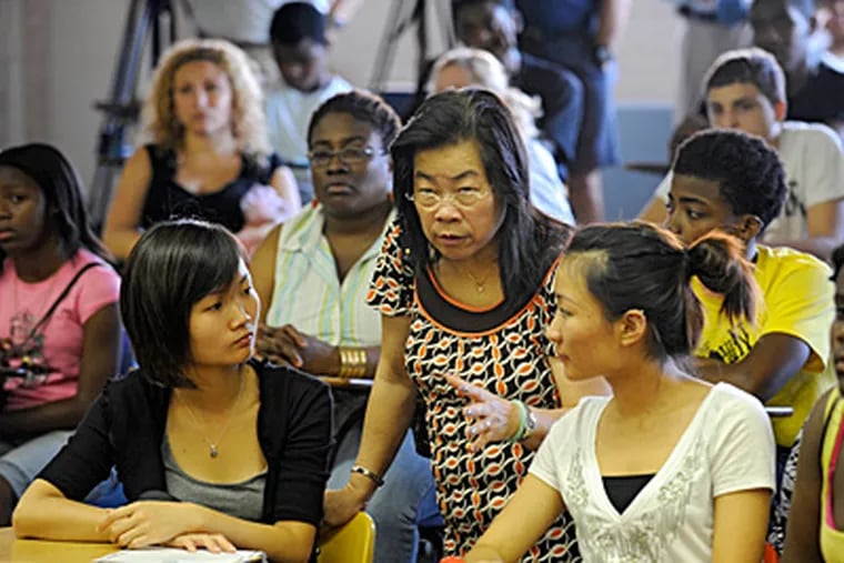 New South Philadelphia High student Mei Hui Huang (right), who came to the U.S. 6 months ago and will be a 10th grader, and her sister Mandy Huang (left) listen to translator Vam Tsang during Tuesday's new student assembly. (Clem Murray/Staff)