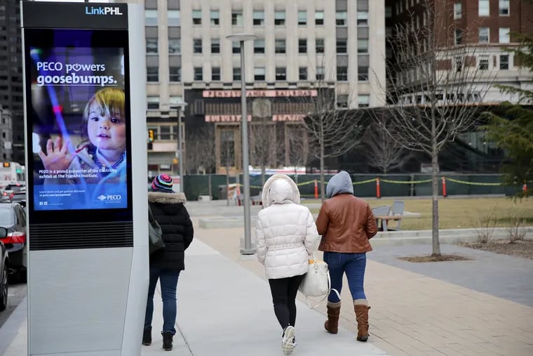 Pedestrians walk by a digital kiosk at 15th and John F. Kennedy Boulevard.